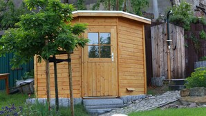 A wooden cabin with a door and windows, surrounded by a garden with a tree and stepping stones. - Apartment "Bauernstube" with pool and sauna use on a restored 3 side courtyard (Meißen)