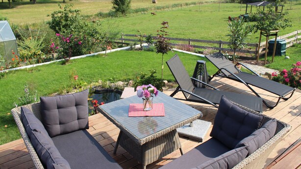A deck with wicker furniture, a small table with a vase of flowers, and a view of a grassy field. - Apartment "Bauernstube" with pool and sauna use on a restored 3 side courtyard (Meißen)