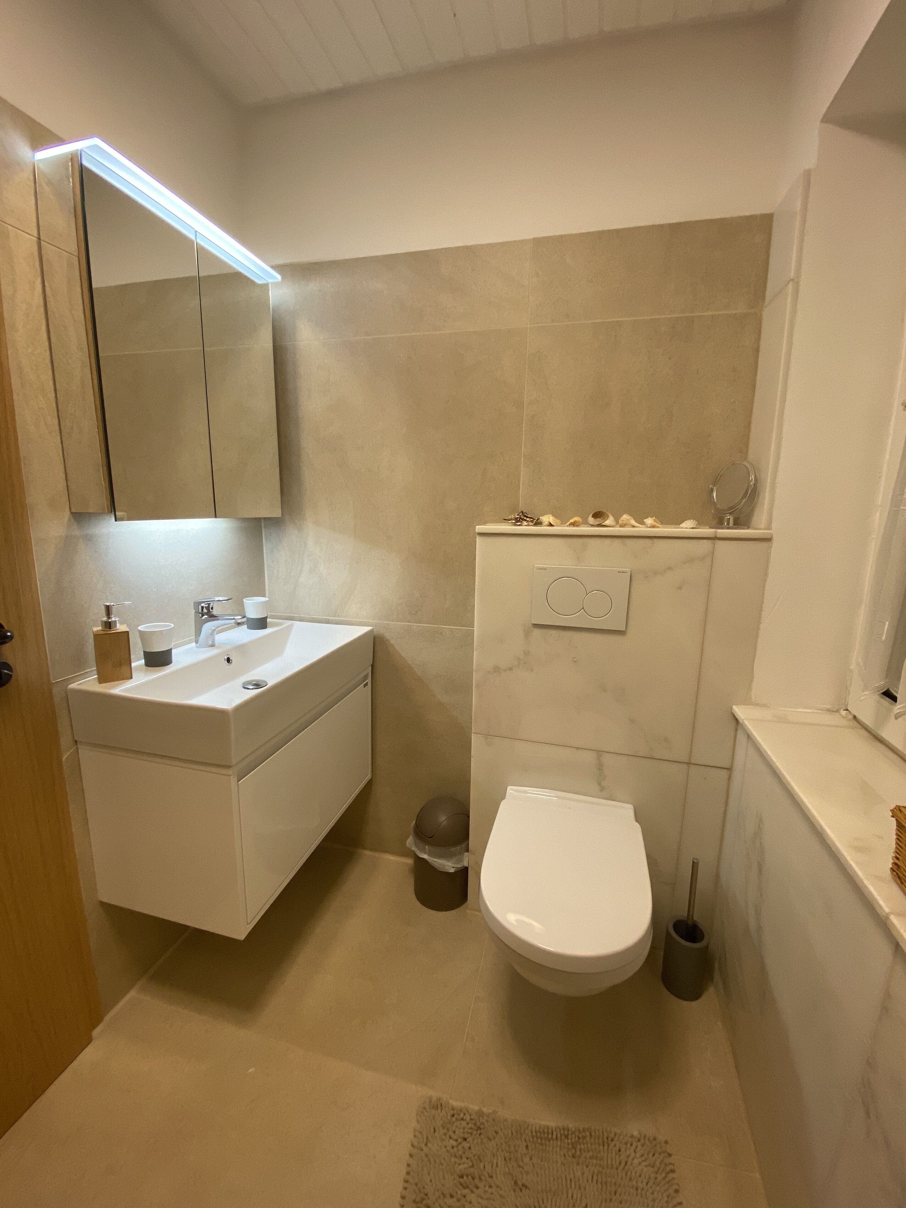 A modern bathroom with a sink, mirror, toilet, and a small trash bin.