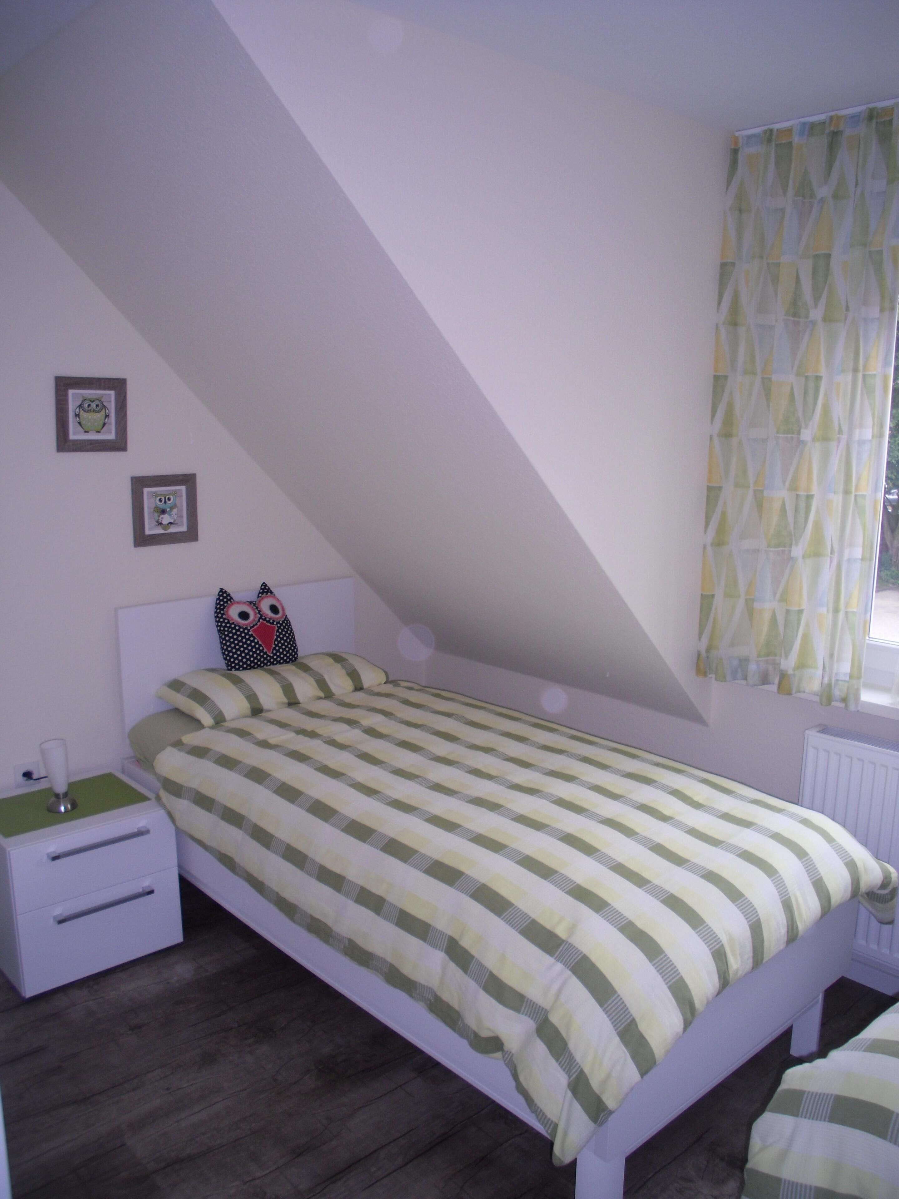 A bedroom with a sloped ceiling, a bed with a striped bedspread, a bedside table with a lamp, and two framed pictures on the wall.