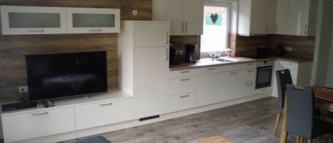 A modern kitchen with white cabinets, a built-in oven, and a large flat-screen TV.