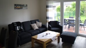 A living room with a black sofa, a wooden coffee table, and a view of a garden through a sliding glass door. - modern, central, quiet area New semi-detached house with a view of the countryside (Horumersiel)