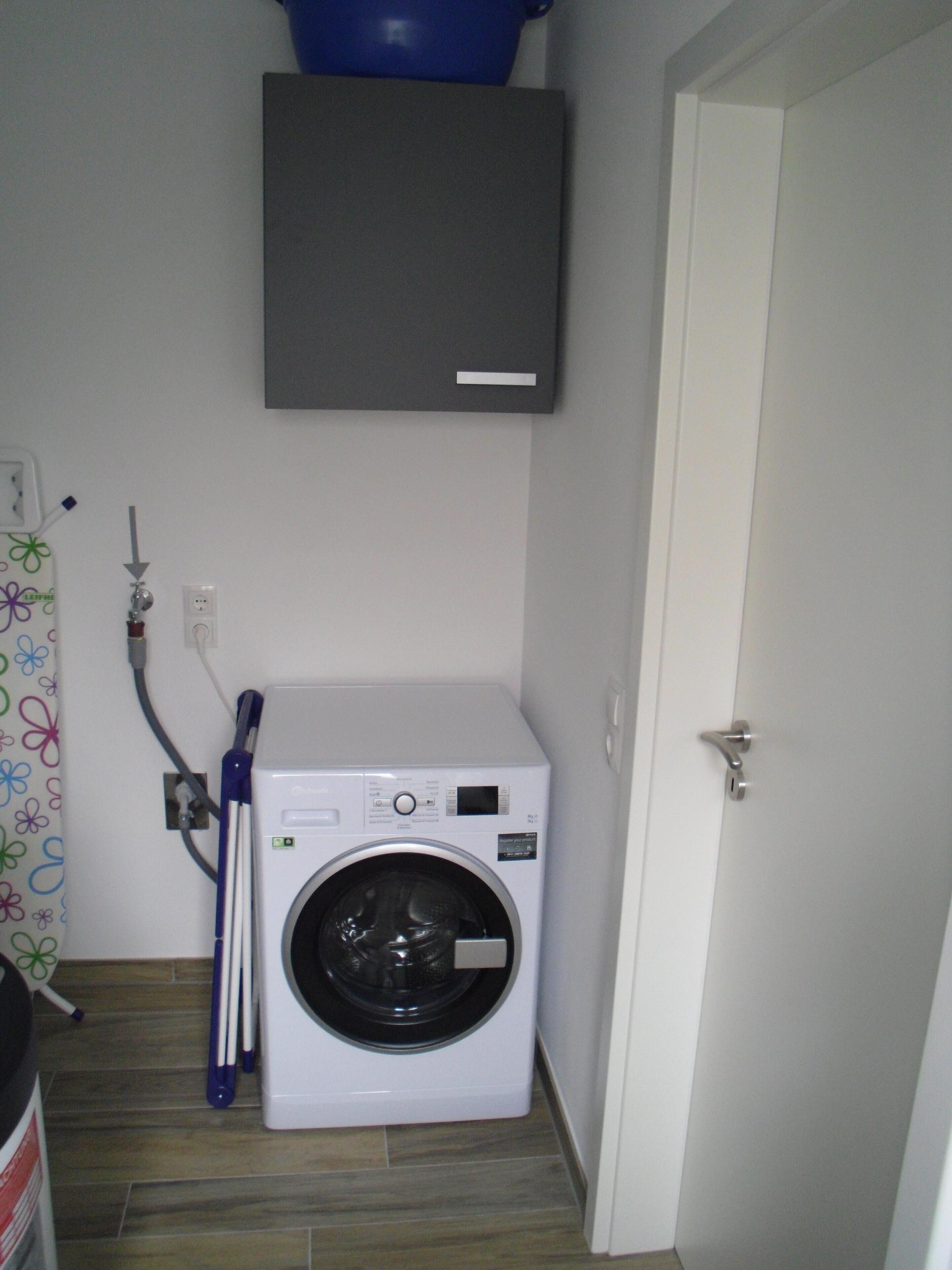 A compact laundry room with a front-loading washing machine, a door, and a wall-mounted cabinet.