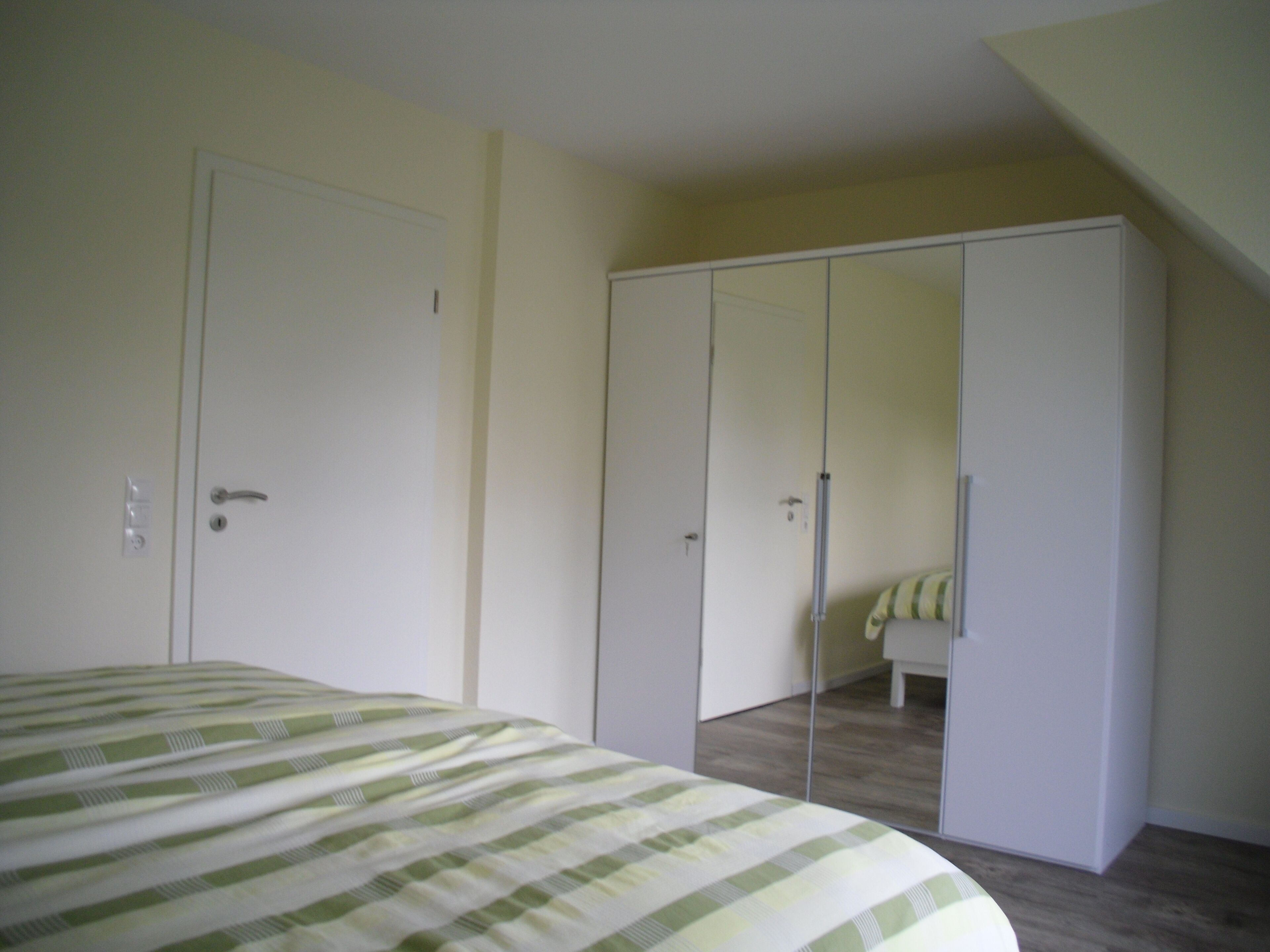 Un dormitorio con cama, armario y espejo.