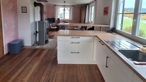 Een ruime keuken met houten vloeren, een ingebouwde kookplaat en een groot raam met uitzicht op de omgeving.