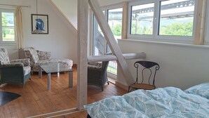 Een kamer met een bed, een bank, een stoel en een tafel. Er zijn ramen en uitzicht op groen.