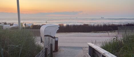 A wooden boardwalk leading to a beach with a white wicker chair and a sign.