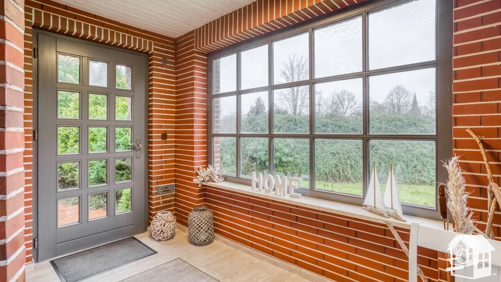 Ein moderner Eingangsbereich mit großem Fenster, einer Tür mit vielen Lichtdurchlässen und einem Willkommensschild.