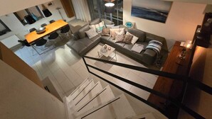 Una sala de estar moderna con un sofá gris, una mesa de comedor de madera y una escalera que sube a otro nivel.