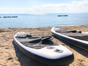 Dos tablas de remo sobre una playa arenosa con un mar tranquilo al fondo.