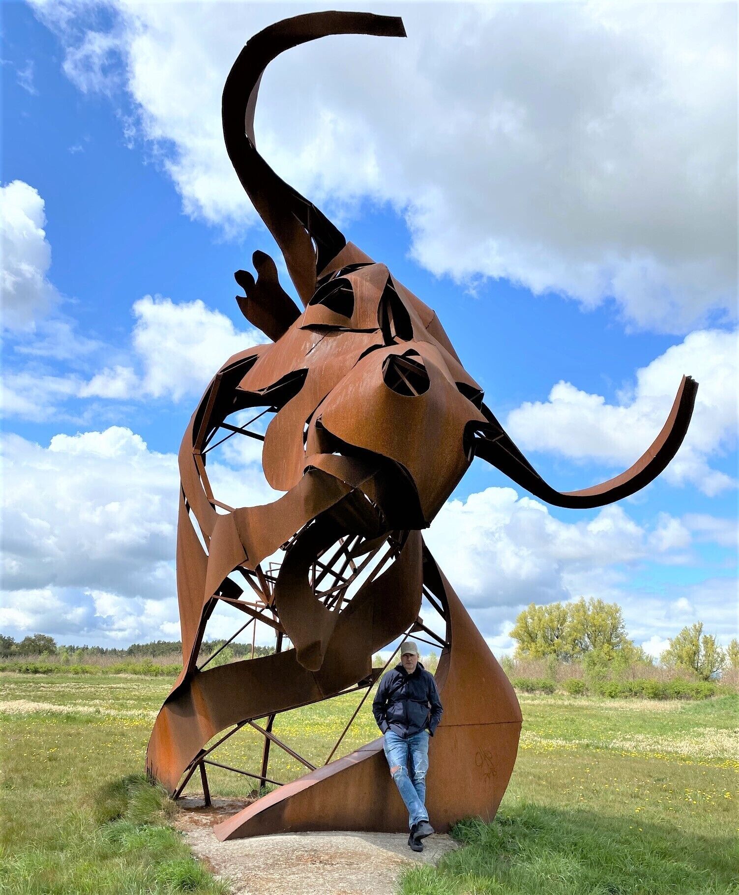 A large metal sculpture resembling a bull in a grassy field with a clear sky.