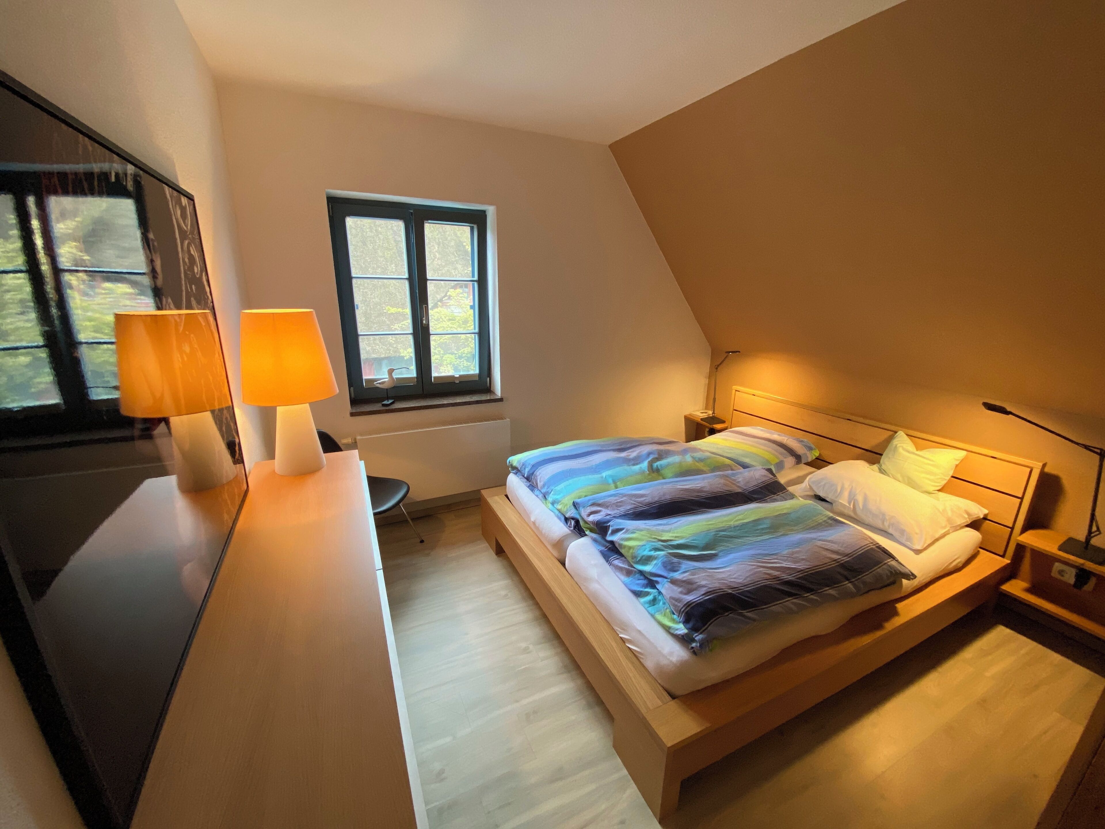 A bedroom with a bed, bedside lamps, a window, and a desk with a lamp.