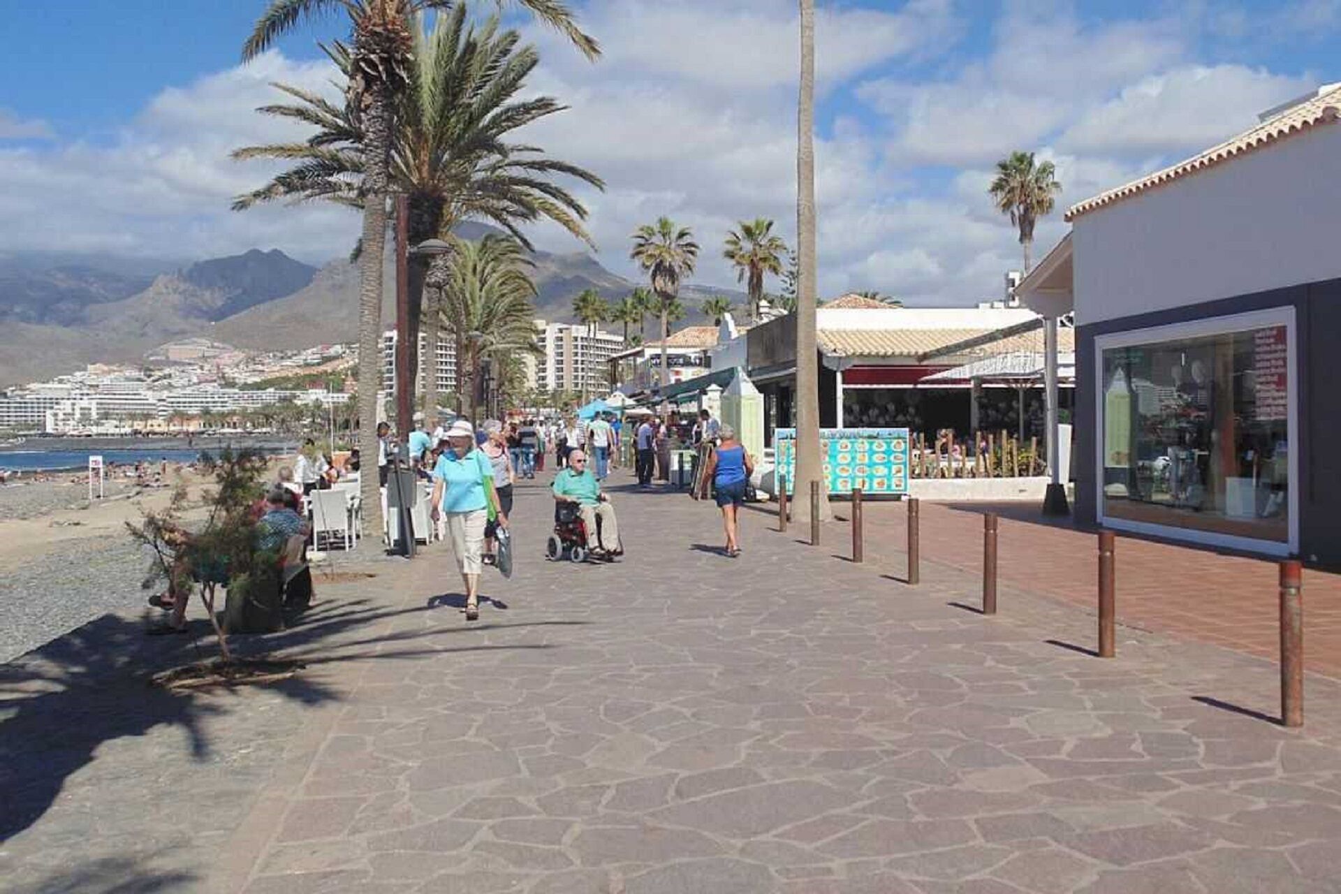 A coastal promenade with palm trees, a beach, and a cruise ship in the background.