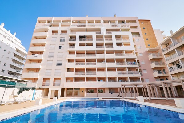 A multi-story hotel with a swimming pool, balconies, and a covered outdoor seating area.