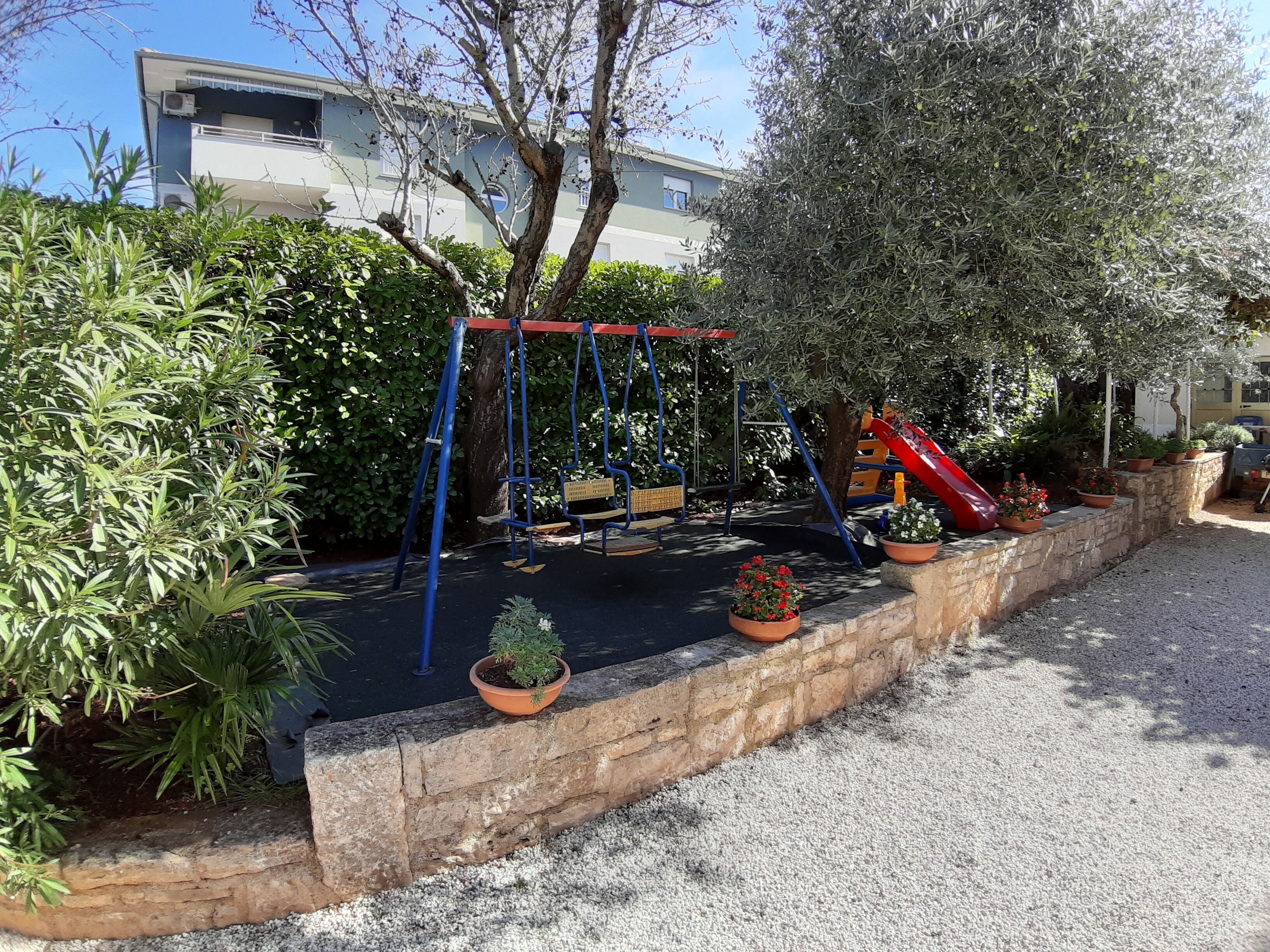 A playground with swings, a slide, and potted plants.