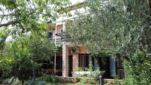 A building with a stone facade, a balcony, and a garden area with trees and shrubs.