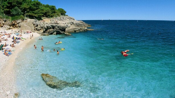 A beach with clear turquoise water, rocky outcrops, and people swimming and sunbathing.