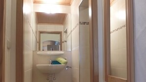 A narrow hallway leading to a bathroom with a sink, mirror, and wooden flooring.