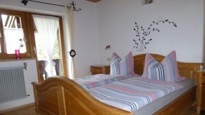 A wooden bed with a striped bedspread, a nightstand, a wall clock, and a window with curtains.