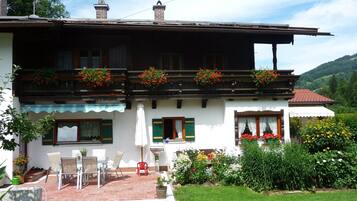 A two-story house with a balcony, a patio with outdoor furniture, and a garden with various plants and flowers.