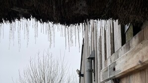 A wooden barn with icicles hanging from the roof, a metal pipe, and a snowy ground.