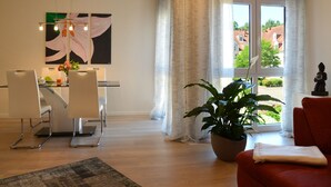 Una sala de estar moderna con comedor, un ventanal con cortinas, una planta en maceta y una estatua.