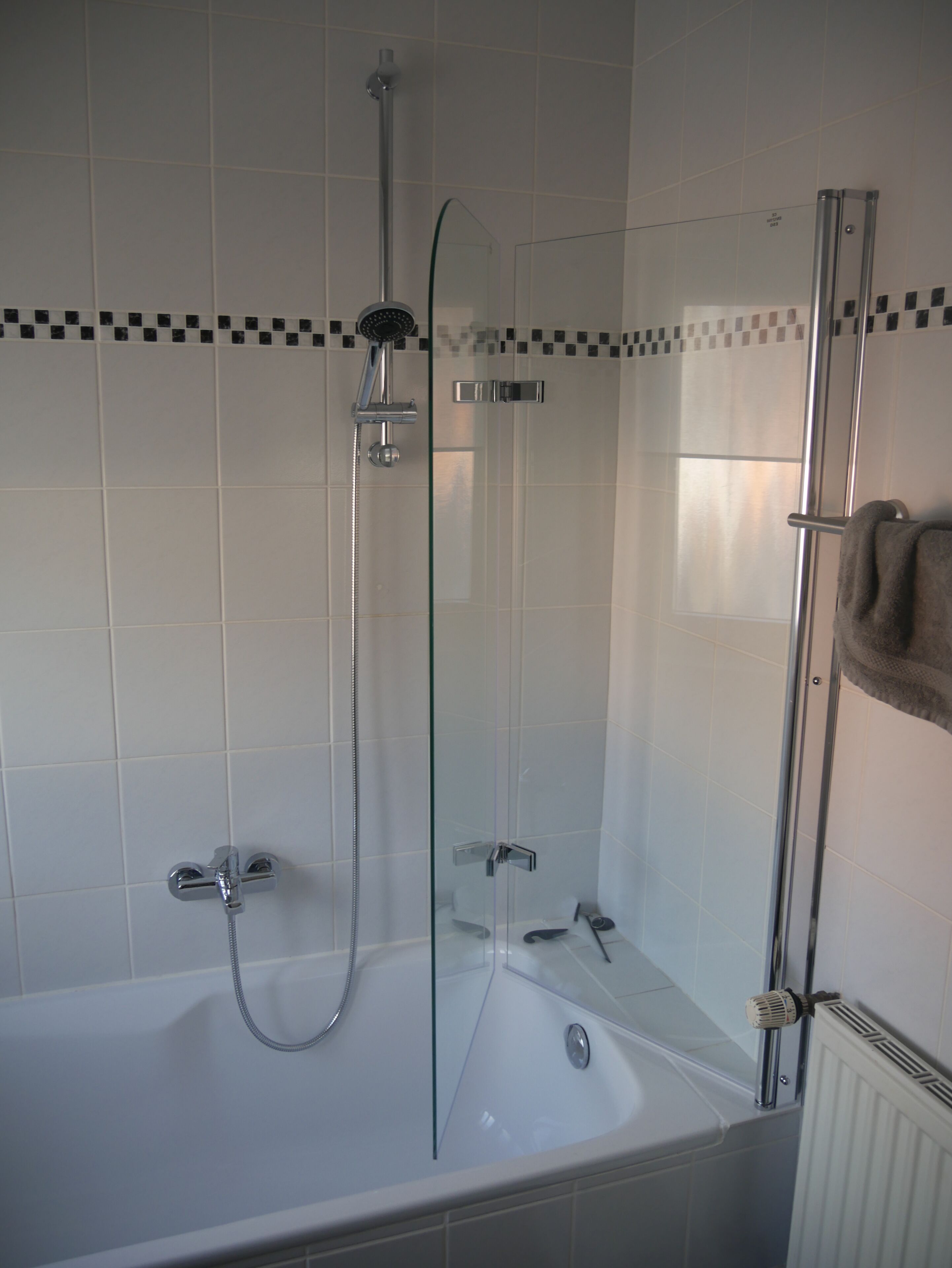 Een moderne badkamer met een douche met glazen wand, een bad en een handdoekhouder.