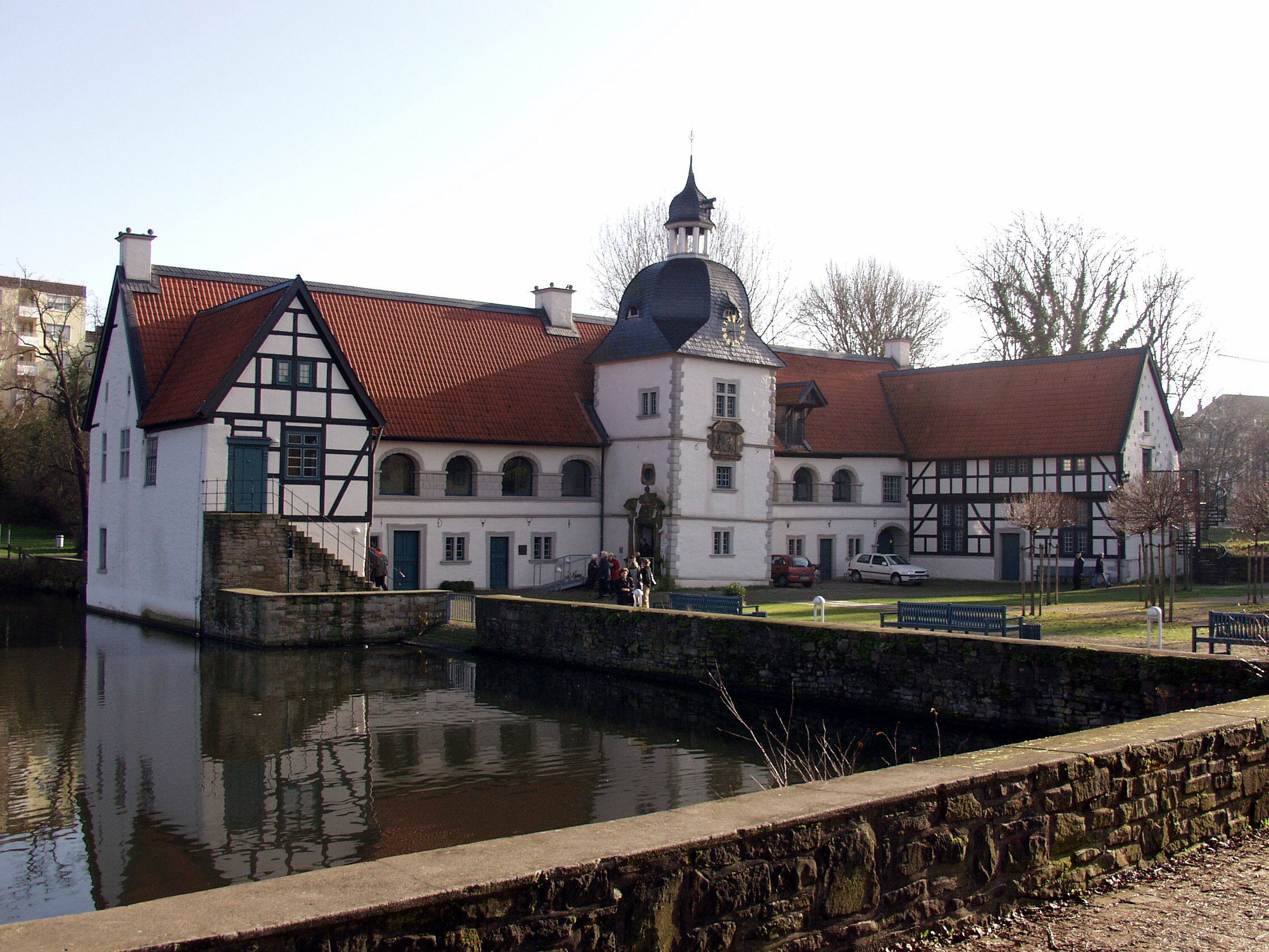 Ein historisches Gebäude mit einem markanten Turm, einem Innenhof und einem Wasserflächen davor.