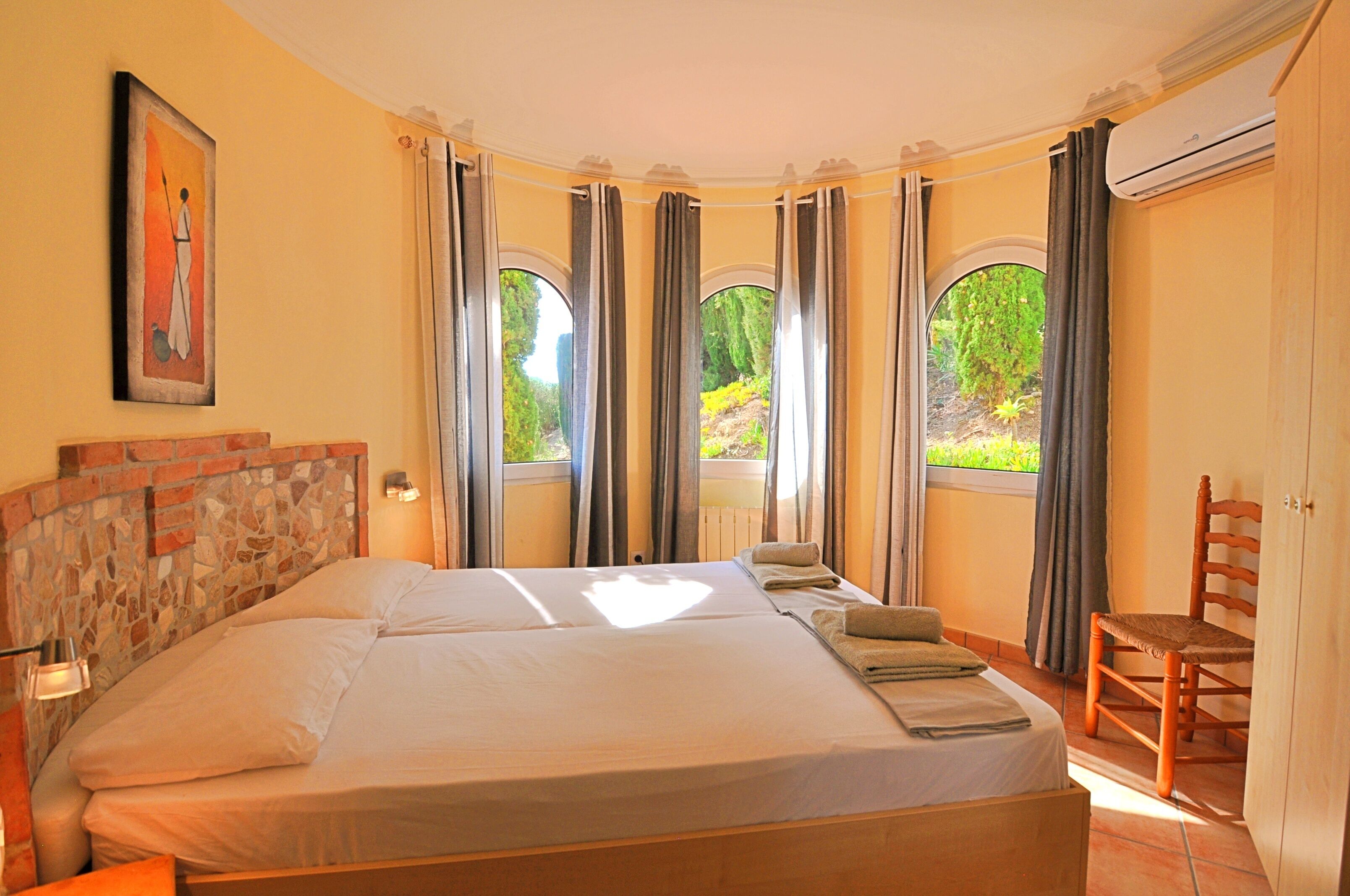 A bedroom with a large bed, a wooden headboard, a chair, and a painting on the wall.