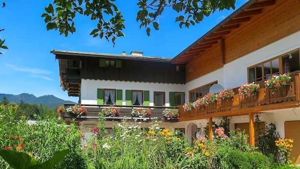 Un bâtiment à deux étages doté d’un balcon orné de fleurs, entouré d’un jardin bien entretenu.