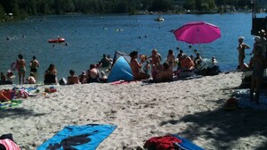Une plage avec des gens, des tentes et des bateaux sur un lac.