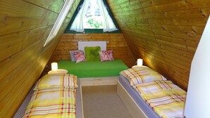 Une petite chambre mansardée, chaleureuse et accueillante, avec deux lits simples, un canapé vert et une fenêtre donnant sur un paysage verdoyant.