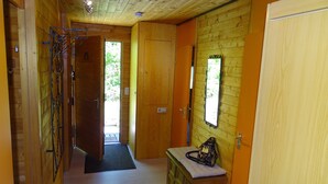 Un couloir intérieur aux murs en bois, avec un banc et une porte donnant sur un espace lumineux.