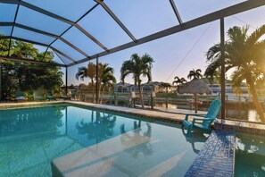 A swimming pool with clear water, surrounded by lounge chairs and palm trees.