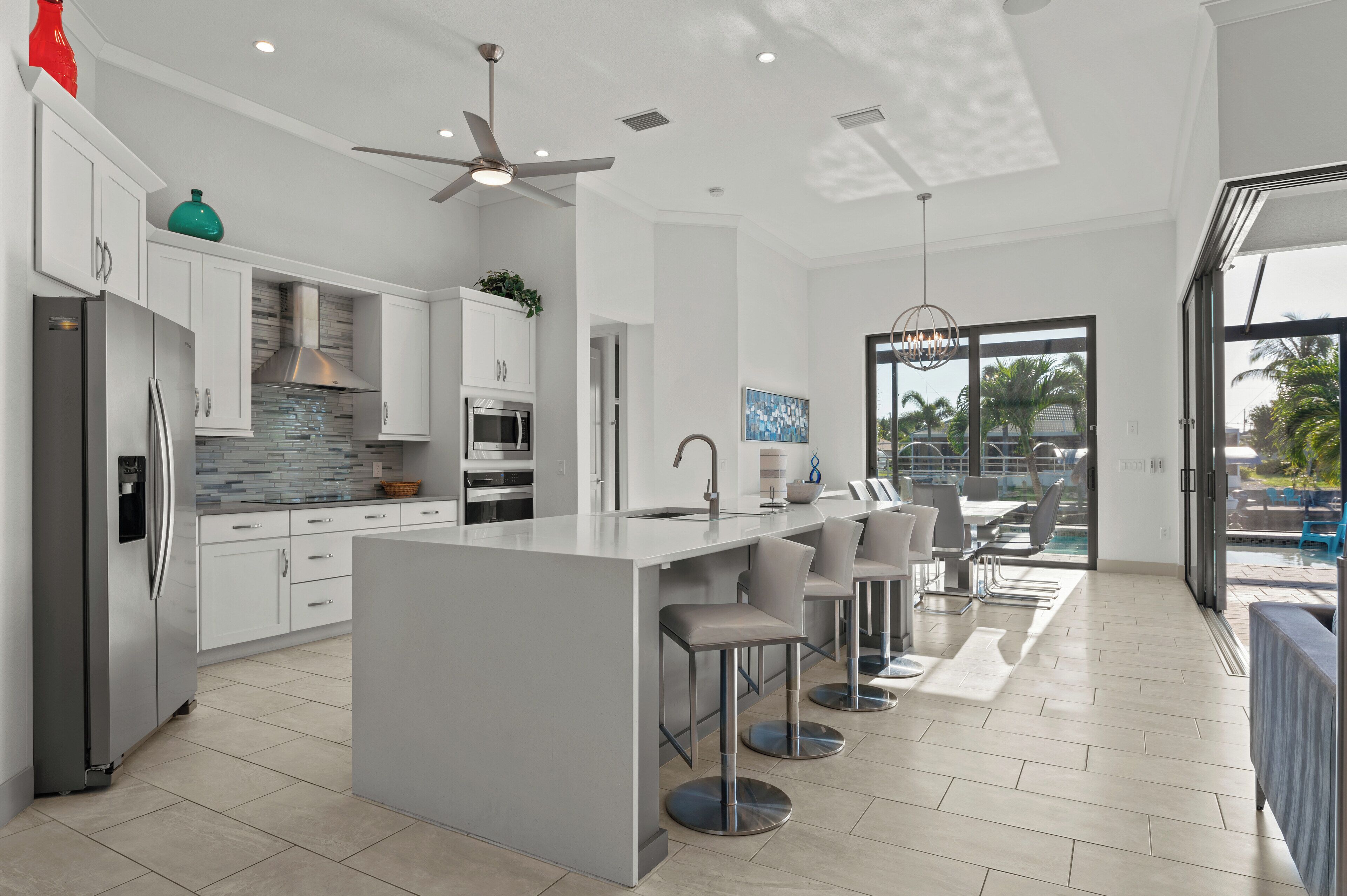 A modern kitchen with a central island, bar stools, and a view of the outdoor pool area.