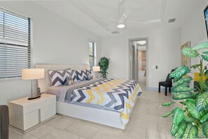 A bedroom with a bed, bedside tables, a lamp, a plant, and a ceiling fan.