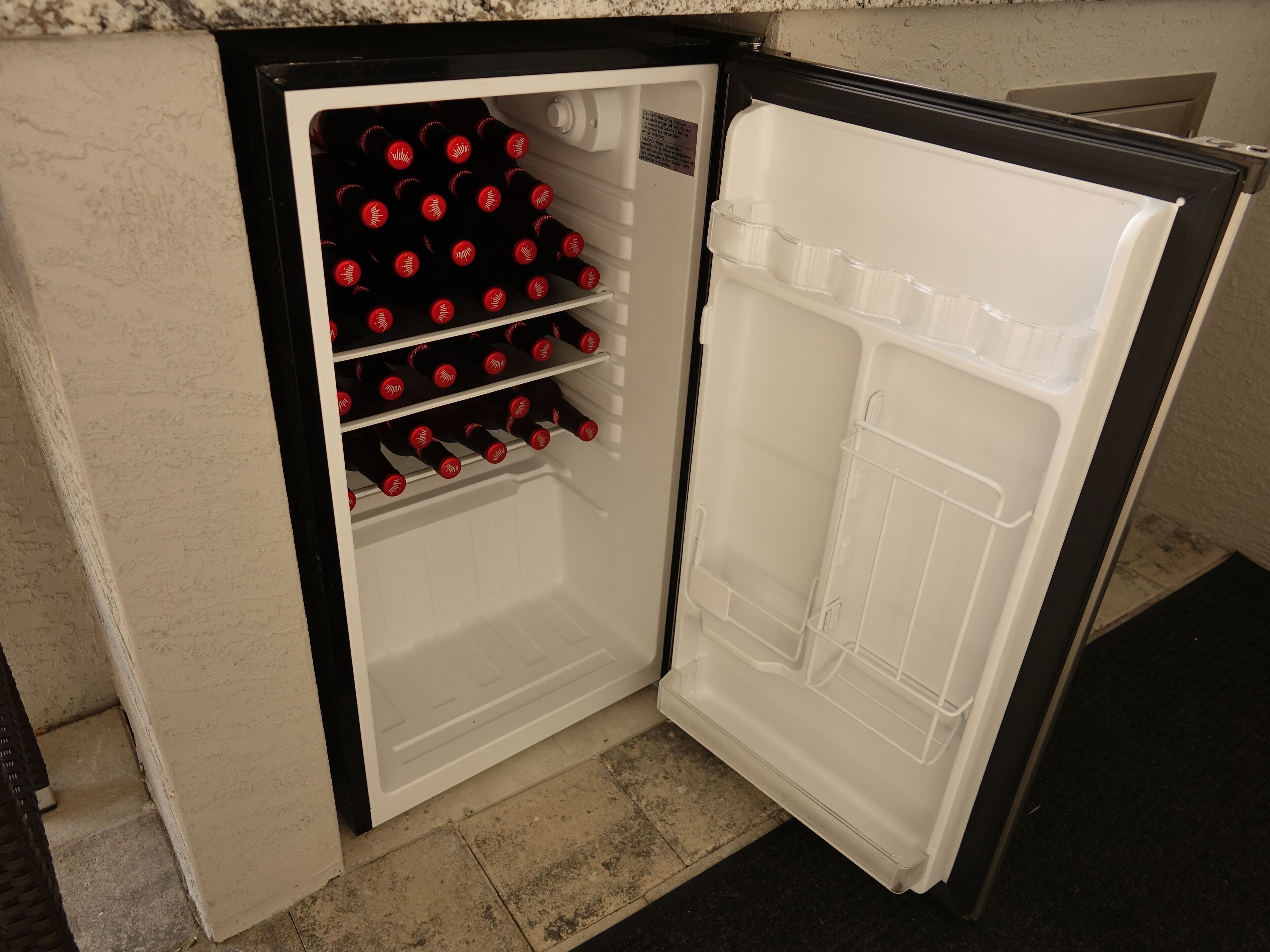 A compact refrigerator with a freezer compartment on top and a main compartment below, containing several bottles.