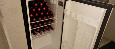 A compact refrigerator with a freezer compartment on top and a main compartment below, containing several bottles.
