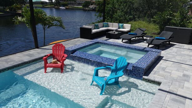Uma piscina com duas cadeiras Adirondack, uma vermelha e outra azul, e uma pequena parte de uma banheira de hidromassagem.