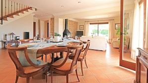 Een eetruimte met een houten tafel voor vier personen, omringd door houten stoelen. Op de achtergrond is een trap te zien die naar een ander niveau leidt.