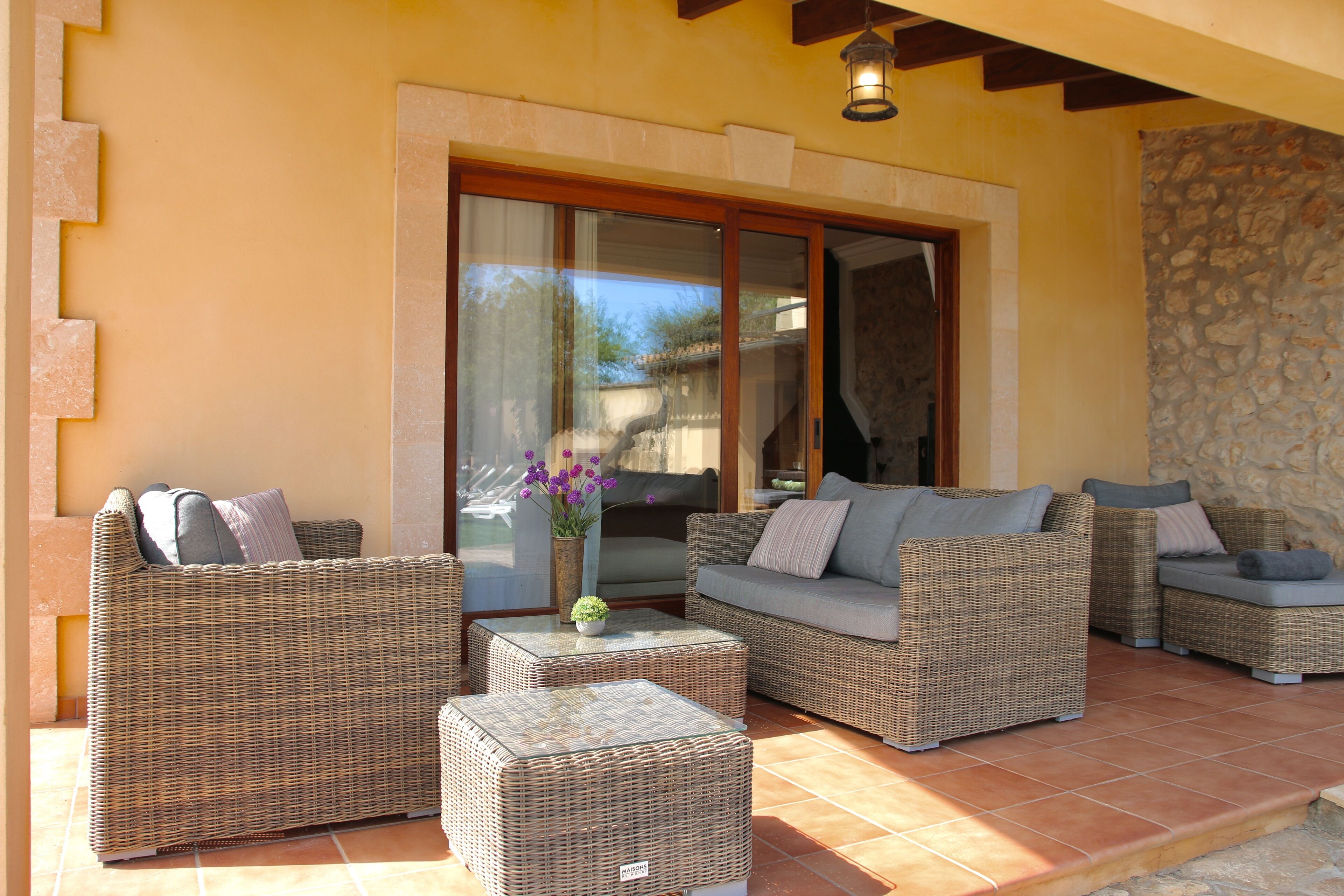 Eine Terrasse mit Korbmöbeln, darunter Sofas, Hocker und ein kleiner Tisch mit Blumen in einer Vase.