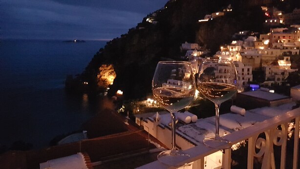 Deux verres à vin sur un balcon donnant sur une ville côtière, de nuit.
