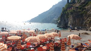 Une plage avec des parasols rayés et des chaises longues, des falaises rocheuses et la mer.
