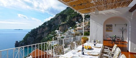 A balcony with a table set for dining, overlooking a coastal town and the sea.