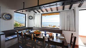 Un espace repas offrant une vue sur la mer, avec une table en bois, des chaises et un banc.
