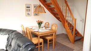 A dining area with a wooden table set for four, surrounded by chairs. A staircase with wooden railings is visible to the right. - Seeschlößchen Thatched Cottage, "Sturmmöwe" Vacation Rental, just 200 meters from the beach (Büsumer Deichhausen)