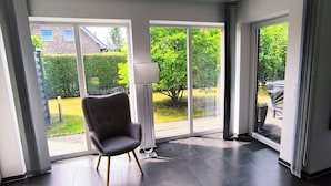 A modern room with large sliding glass doors, a dark grey upholstered chair, and a floor lamp. - Fantastic holiday home on the left Lower Rhine between the Rhine and Wisseler See (Kalkar)