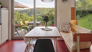 A room with a table, chairs, a bench, a vase with flowers, and a view of a forest through a large window. - Architect-designed house, wooden house on a 10,000 m² lot of meadows and woods with a panoramic view (Schutz)