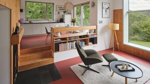 A modern interior with a kitchen, dining area, and a large window offering a view of greenery. - Architect-designed house, wooden house on a 10,000 m² lot of meadows and woods with a panoramic view (Schutz)