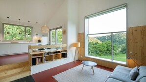 A modern interior with a kitchen, dining area, and a large window offering a view of greenery. - Architect-designed house, wooden house on a 10,000 m² lot of meadows and woods with a panoramic view (Schutz)